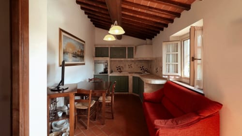 Appartamento rustico a Borgo di Erboli a Cavriglia con divano rosso, travi in legno, cucina e zona pranzo