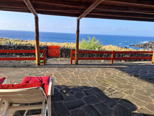 Red cushioned lounge chair on stone terrace with wooden pergola overlooking blue ocean at Inn Nature villa in São Roque do