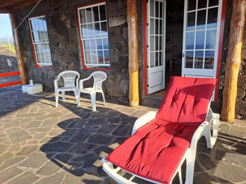 Sunny patio at Inn Nature villa in São Roque do Pico with red loungers, white chairs, and sea views