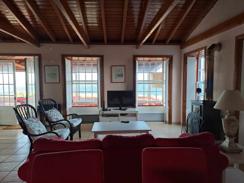 Spacious sea-view villa living room at Inn Nature with burgundy seating, wooden beams, ocean views through large windows, and