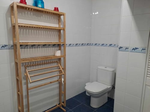 Bathroom at Inn Nature villa with wooden shelving, white tiles, blue dolphin border, and toilet in São Roque do Pico