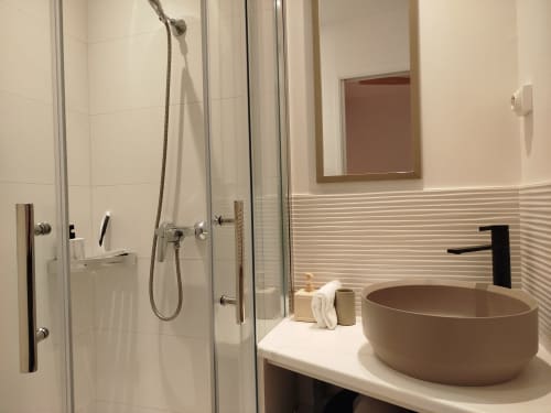Salle de bains moderne à la Villa Voltaire avec lavabo rond beige, douche vitrée et carrelage aux teintes neutres