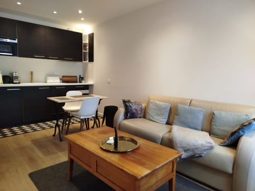 Séjour ouvert moderne à la Villa Voltaire avec canapé beige, table basse en bois et kitchenette noire à Clamart