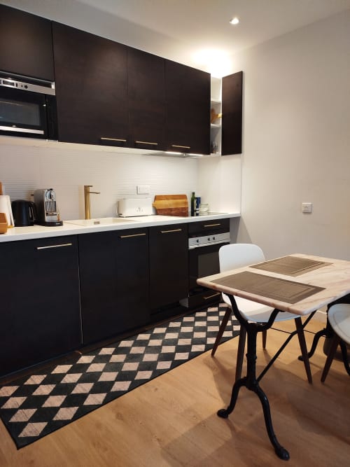 Cuisine noire moderne avec plan de travail blanc, table à manger et carrelage à motifs géométriques dans l'appartement La Suite Emilie à Villa