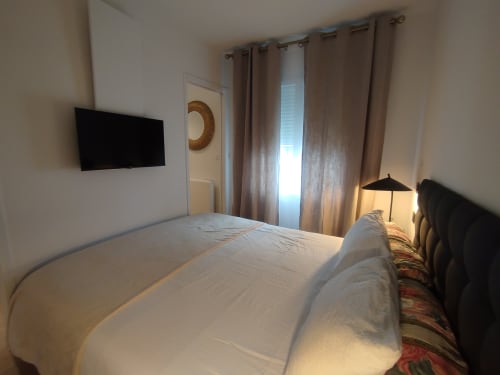 Chambre moderne de la Villa Voltaire à Clamart avec lit blanc, TV murale et rideaux beige
