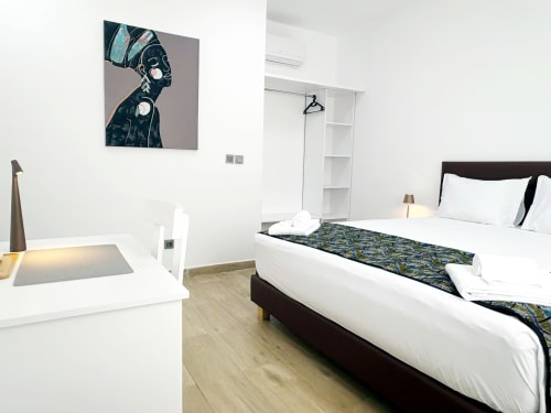 Habitación moderna del hotel Dakar By Days con obras de arte, ropa de cama blanca, cabecero oscuro y muebles contemporáneos