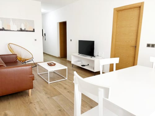 Sala de estar moderna del hotel Dakar By Days con sofá de cuero marrón, puertas de madera, televisor y mobiliario blanco minimalista