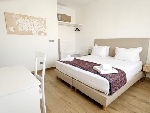 Habitación moderna en el hotel Dakar By Days con cama beige, almohadas blancas, piso de madera y arte floral en la pared en Dakar.