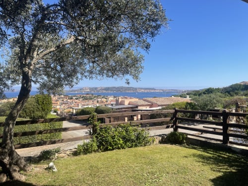 Palau sea view garden with olive tree, wooden fence, and blue Mediterranean water and coastal town below