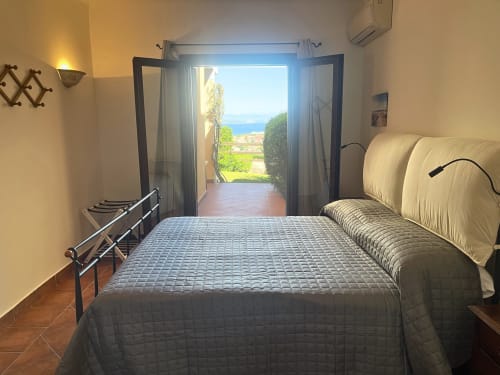 Sea View Garden room at Like at Home Palau with bed, balcony doors opening to Mediterranean vista and garden