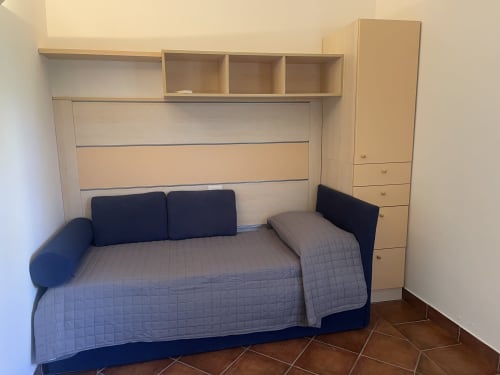 Modern bedroom at Like at Home Palau with blue sofa bed, wood storage furniture, and neutral walls