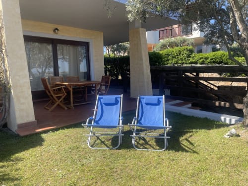 Blue beach chairs on garden lawn facing patio with dining table at Like at Home Palau, Sardinia
