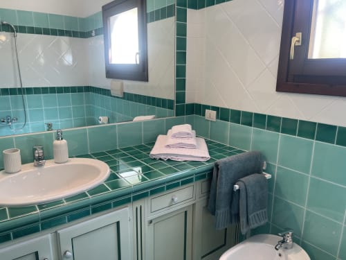 Bathroom with turquoise tile walls, sink, bathtub, and towel rack at Like at Home Palau hotel apartment