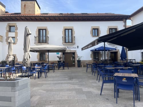 Patio del hotel Casa Azcona en Zizur Mayor con sillas azules, sombrillas y fachada de piedra blanca