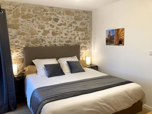 Dormitorio moderno en Au Château De Villelongue con pared de acento de piedra, cama queen, cabecero oscuro y decoración arquitectónica