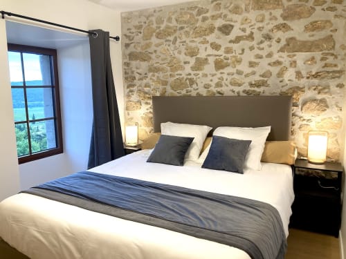 Habitación La Suite de la Citadelle en Au Château De Villelongue con muros de piedra, vista a la montaña y mobiliario moderno.