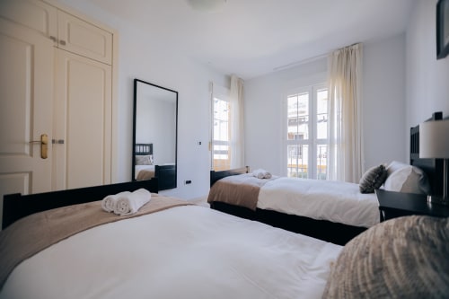 Modern twin bedroom at Itaca by BH Marbella with sea view balcony, black beds, cream wardrobes, and contemporary decor