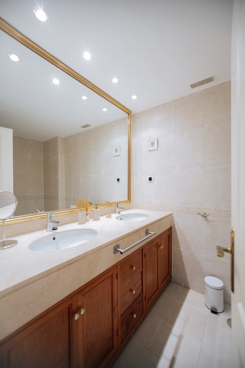 Modern bathroom at Itaca by BH Marbella with dual vanity sinks, gold-framed mirror, and wooden cabinets