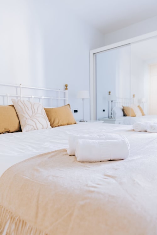 Luxurious bedroom at Itaca by BH Marbella with white bedding, gold pillows, and rolled towels on bed