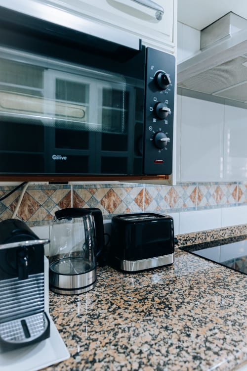 Modern kitchen area in Itaca apartment at BH Marbella with black microwave, toaster, and coffee maker on speckled countertop