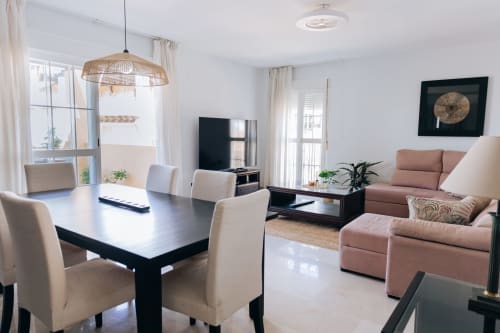 Modern open-plan living room at Itaca by BH Marbella with dining table, sea-view balcony, TV, and terracotta sofa