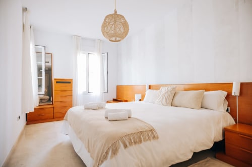 Bright bedroom at Rodas by BH Marbella with two beds, wooden furniture, woven pendant light, and garden view