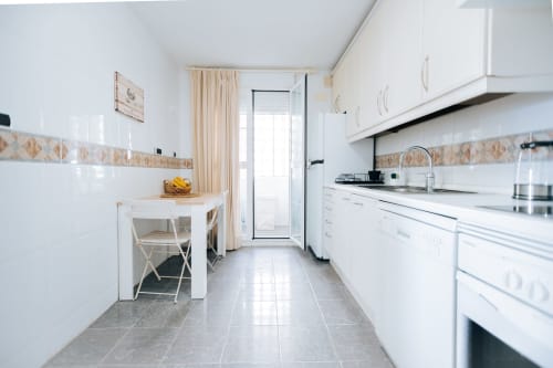 Modern white kitchen with dining area at Rodas by BH Marbella apartment, featuring appliances and garden view access