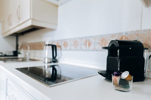 Modern kitchen in Rodas by BH Marbella apartment with white counters, black coffee machine, and decorative tile backsplash