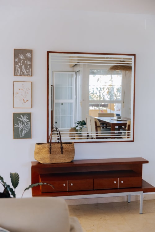 Modern entryway at Rodas by BH Marbella with wooden console, woven basket, framed botanical art, and mirror with garden view