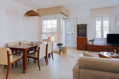 Bright open-plan living area at Rodas by BH Marbella with dining table, sofa, TV, and garden views through large windows