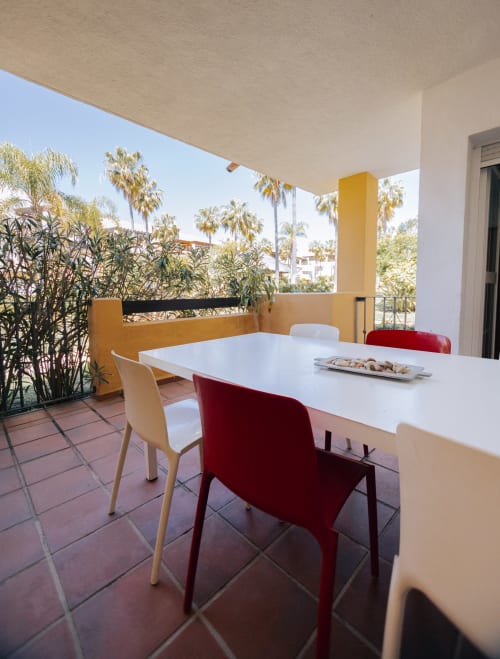 Sunny balcony at Rodas by BH Marbella with white dining table, colorful chairs, and palm tree views