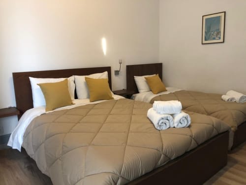 Quarto triplo na Pousada Infante Dom Henrique em Coimbra com duas camas, almofadas douradas, toalhas enroladas e móvel em madeira escura