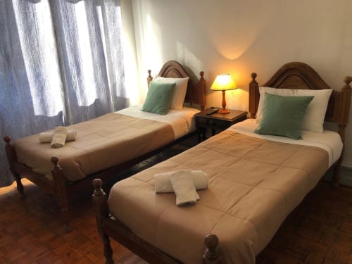 Quarto duplo na Guest House Infante Dom Henrique em Coimbra com camas de madeira, almofadas verdes e luz natural das cortinas