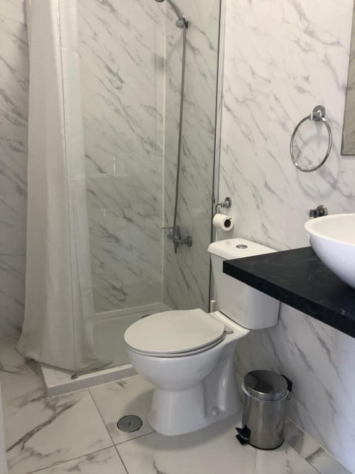 Banheiro moderno com azulejos de mármore, vaso sanitário branco, cuba de louça, box de vidro e metais cromados na Pousada