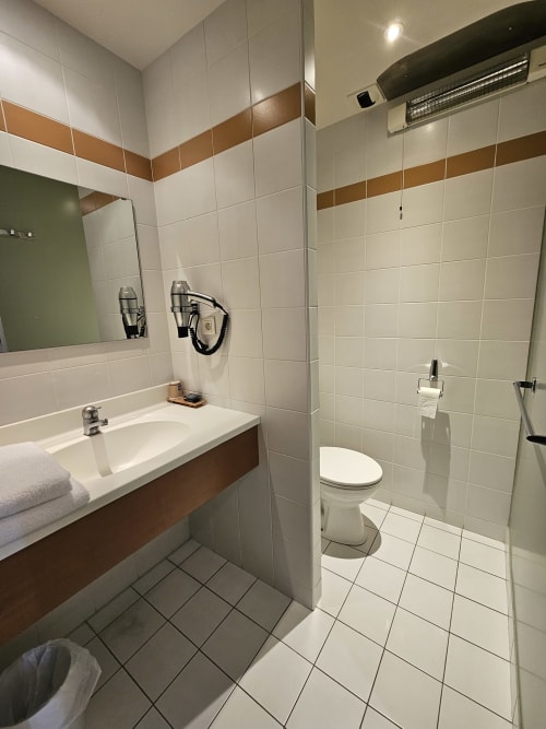 Salle de bain moderne aux carreaux blancs, bande d'accent marron, vasque, toilettes et douche à l'italienne à l'Hôtel La Route