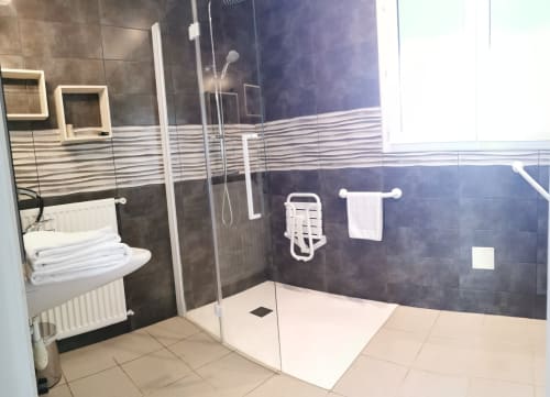 Salle de bains accessible à l'Hôtel La Route d'Argent à Bozouls avec douche à l'italienne, porte-serviettes chauffant et barres de soutien.