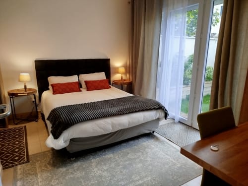 Chambre moderne à la Villa Voltaire avec vue sur le jardin, tête de lit noire, coussins rouges, bureau et portes-fenêtres à Clamart
