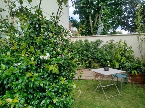 Terrasse du jardin de l'appartement Villa Voltaire avec table, chaises et végétation luxuriante à Clamart