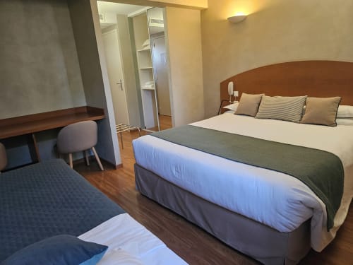 Chambre triple de l'Hôtel La Route d'Argent à Bozouls avec deux lits, bureau en bois, armoire miroir et éclairage chaleureux
