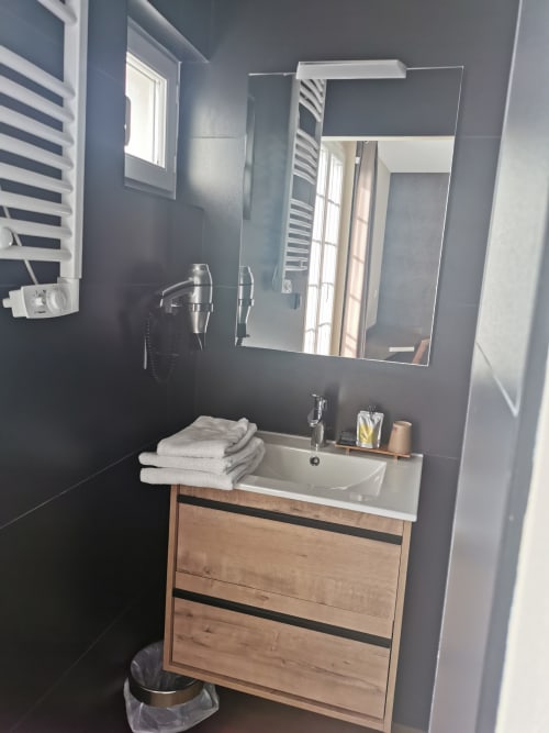 Salle de bain moderne à l'Hôtel La Route d'Argent à Bozouls avec meuble en bois, lavabo blanc, miroir et radiateur sèche-serviettes