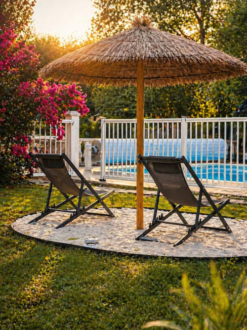 Deux chaises longues noires sous un parasol en paille près de la piscine de La Biche Au Bois, gîte à Moncléra, France