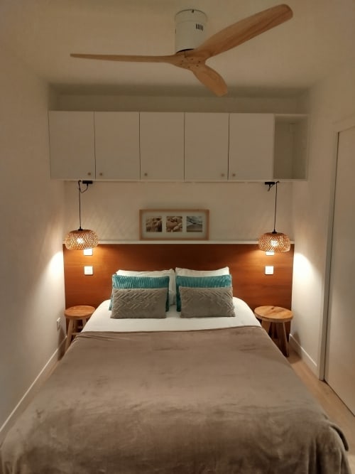 Chambre moderne de la Villa Voltaire Clamart avec tête de lit en bois, ventilateur de plafond, luminaires suspendus et vue sur le jardin