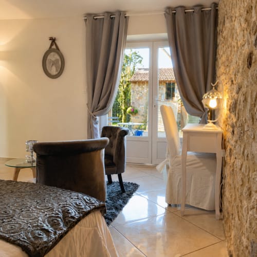 Élégante chambre de La Biche Au Bois B&B à Moncléra avec fauteuil cuir marron, mur en pierre et vue sur le jardin