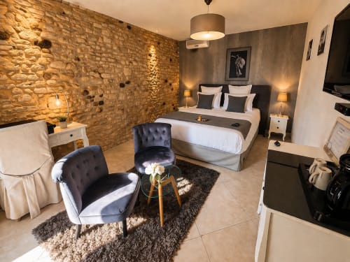 Chambre de luxe à La Biche Au Bois à Moncléra avec murs en pierre, lit moderne, coin salon et vue sur le jardin