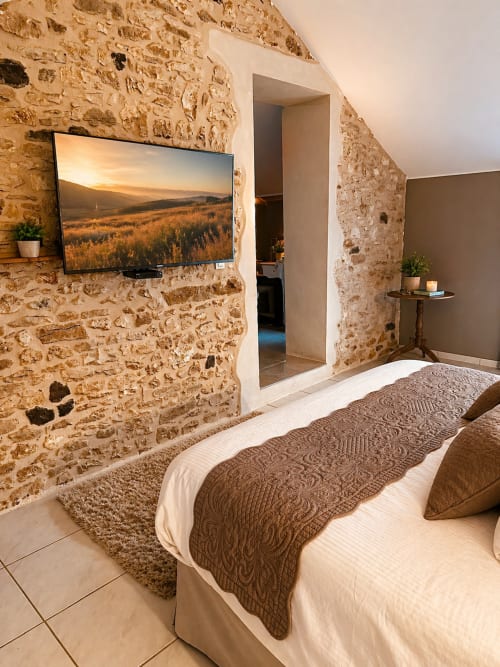 Chambre Suite la Cazalaise à La Biche Au Bois avec murs en pierre apparente, lit et TV murale à Moncléra