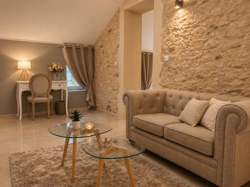 Suite élégante à La Biche Au Bois avec murs en pierre, canapé beige, tables en verre et décor rustique français à Moncléra