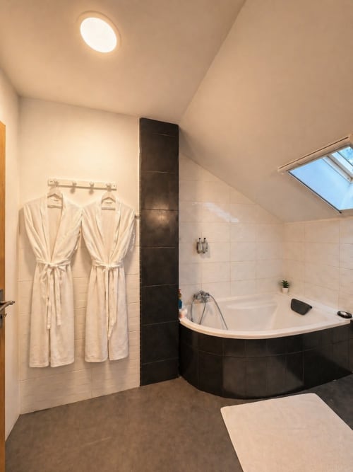 Salle de bain moderne de la Suite la Cazalaise à La Biche Au Bois avec baignoire d'angle, peignoirs crème et puits de lumière