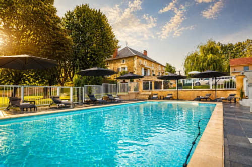 Piscine étincelante du gîte La Biche Au Bois à Moncléra, France, avec transats et bâtisse en pierre