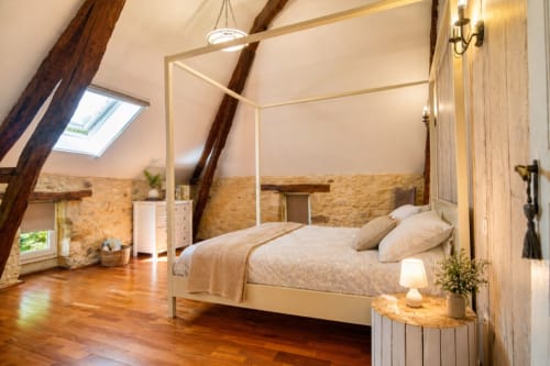 Spacieuse chambre au Gîte Le Tranquille avec lit à baldaquin, poutres apparentes, murs en pierre et parquet à La Biche Au