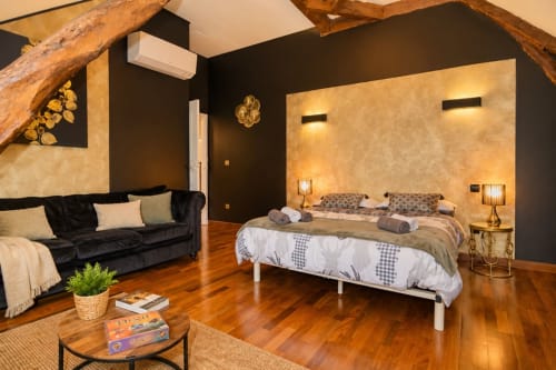 Chambre spacieuse du cottage La Biche Au Bois à Moncléra avec lit double, canapé noir, poutres apparentes, parquet